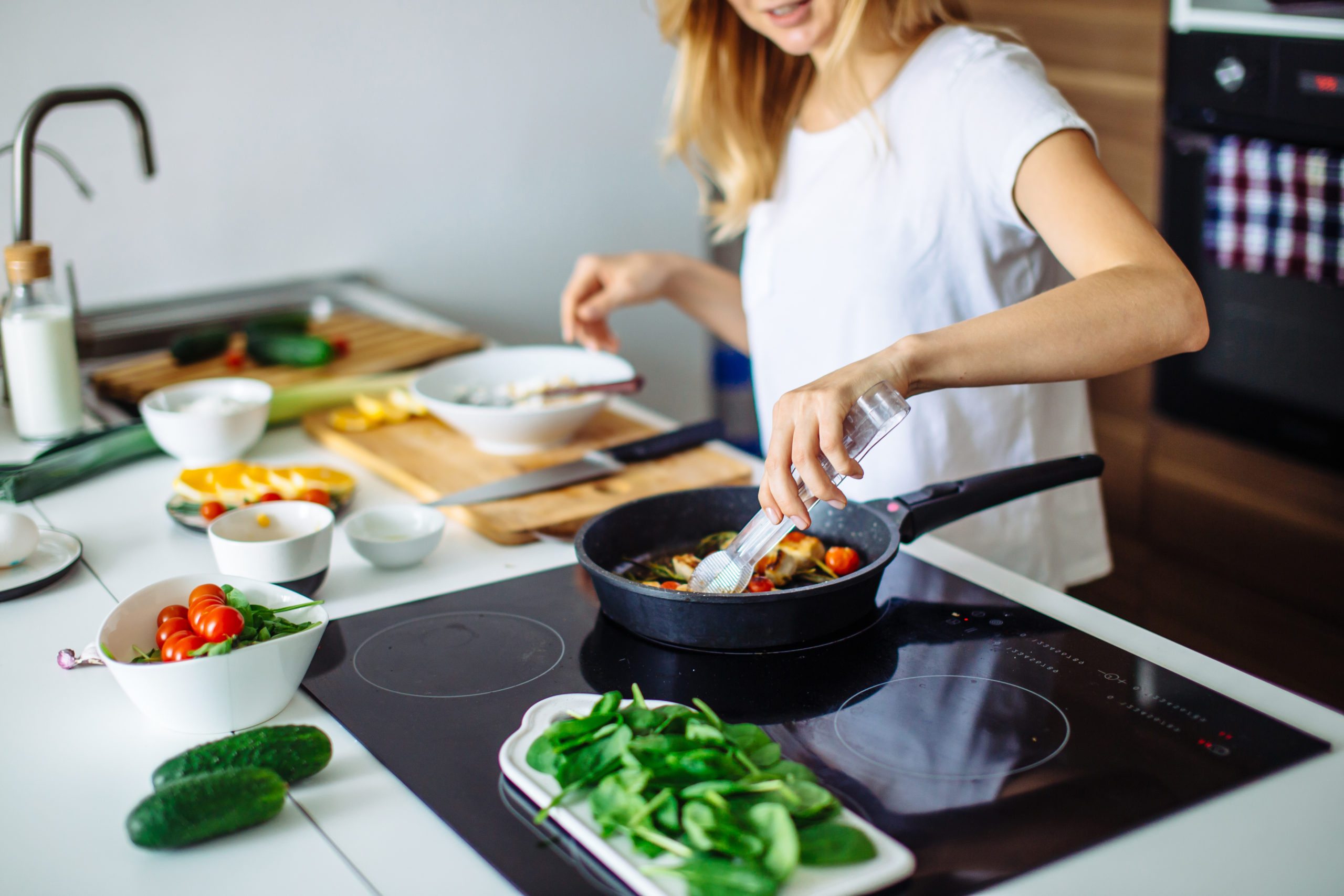 Jeune femme en train de cuisiner à l'aide d'une casserole et d'une cuillère en bois, sur une plaque de cuisson.